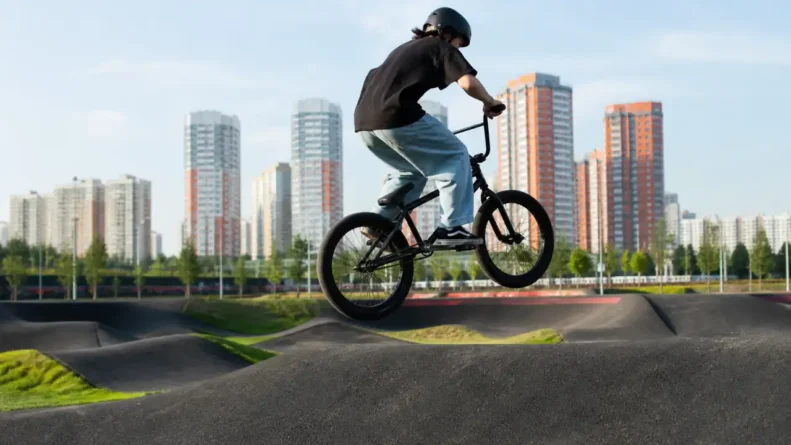 Велосипедист в шлеме выполняет прыжок на BMX на открытой площадке