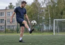 Спортсмен подбивает футбольный мяч стопой на открытой площадке